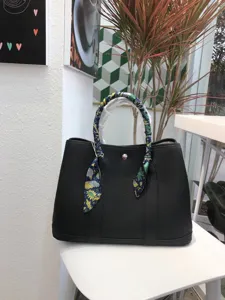 Vista dettagliata della borsa tote in pelle nera con manico avvolto in foulard di seta.