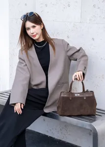 Detail view of the brown suede handbag featuring a classic turn lock and sturdy top handle.