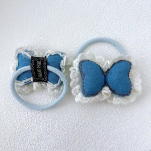 Vue détaillée de l'élastique cheveux en denim pour enfant avec dentelle blanche et nœud.