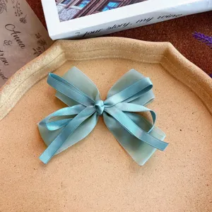 Close-up detail of a sweet sage green ribbon bow hair clip with flowing tails on tray.