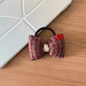 Primo piano dettaglio del legatutto per capelli a quadri rosso e grigio con bottone rosso.