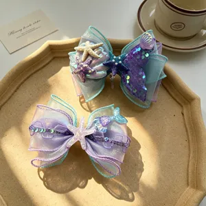 Mermaid bow hair clip detail shot, showing cute seashell starfish and shiny sequin mesh designs.