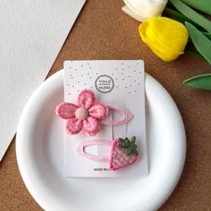 Gros plan de jolies pinces à cheveux en tissu rose fleur et fraise sur carte blanche, doux.
