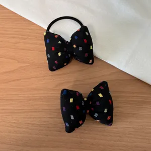 Close-up detail of black bow hair tie with colorful woven pattern and elastic rubber band.