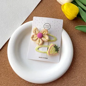 Gros plan détaillé de pinces à cheveux en tissu fleurs et fraises à carreaux jaunes.