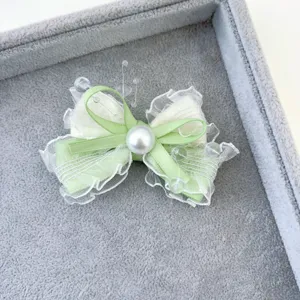Dettaglio ravvicinato della molletta per capelli a fiocco verde chiaro con pizzo e perla.