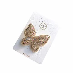 Nahaufnahme Detail einer goldenen Schmetterlings-Haarspange mit bunten Sternen auf Karte.