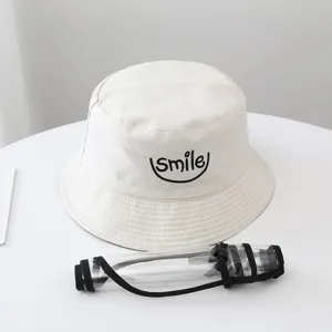 Detail view of the white bucket hat featuring detachable transparent face shield and smile embroidery.