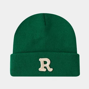 Gros plan d'un bonnet en maille vert foncé montrant la lettre R brodée sur le revers épais.
