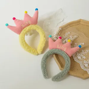 Detailed view of plush crown headband with colorful pom poms and cute embroidered design.