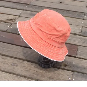 Washed vintage bucket hat detail, coral red cotton fabric with white edge for sun protection.