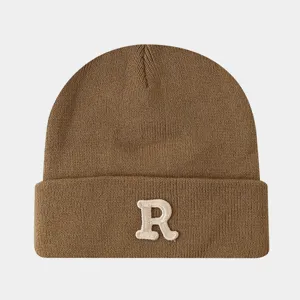 Vue en gros plan détaillée du bonnet d'hiver marron en tricot avec la lettre R brodée.