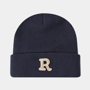 Gros plan détaillé du bonnet en tricot bleu marine avec un élégant motif de lettre R brodé.