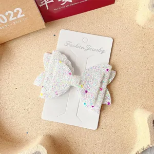 Glitter bow hair clip detail view showing sparkling sequin texture and display card packaging.