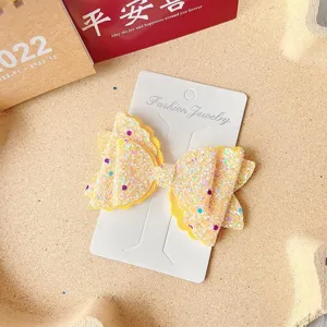 Glitter bow hair clip detail shot, sparkling sequin bow design on display card for kids.
