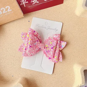 Close-up detail of the sparkling pink glitter bow hair clip on white display card.