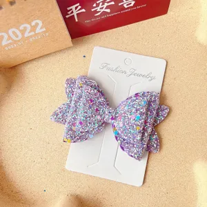 Close-up detail of the purple glitter bow hair clip, showing the sparkly sequin texture.