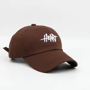 Detalle de gorra de béisbol marrón con texto HEART bordado en blanco y tela limpia.