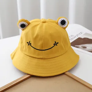 Detail shot of cute yellow bucket hat featuring 3D frog eyes and black smile embroidery.