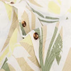 Close-up detail showing the tropical leaf print and brown button on the summer shirt.