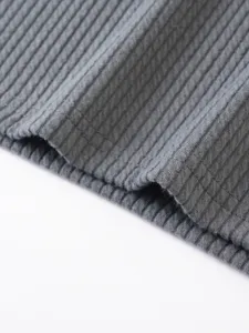 Grey ribbed knit fabric detail close up showing vertical stripes texture and hem stitching.