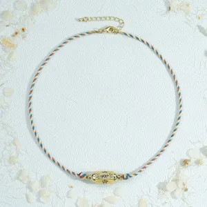 Close-up detail shot of colorful braided cord necklace featuring a gold hexagonal pillar pendant.