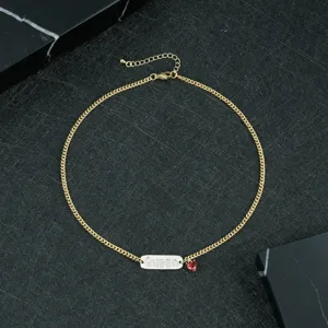 Gold tone necklace featuring a zircon paved Queen plaque pendant and a red heart drop.