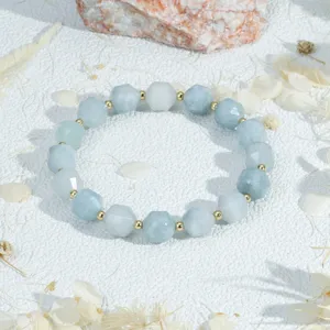 Close-up detailweergave van lichtblauwe gefacetteerde edelsteen en gouden kraal stretch armband.