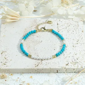 Close-up detail of beaded bracelet featuring turquoise and faux pearls on stone slab.