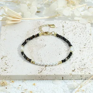Delicate beaded bracelet featuring dark faceted stones and white faux pearls with gold accents.