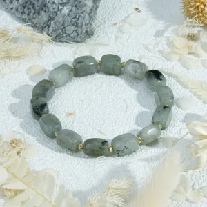 Close-up irregular grey-green stone bead bracelet with gold spacers on a white textured background.