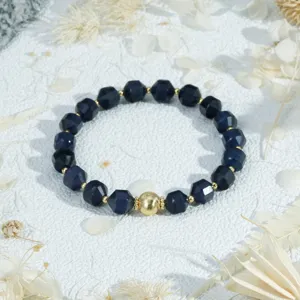 Detailed close-up of a deep blue faceted beaded bracelet with a central gold bead, elegant style.