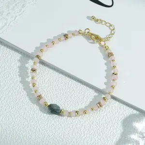 Primer plano detallado de la elegante pulsera de cuentas rosadas con detalles dorados y cadena.