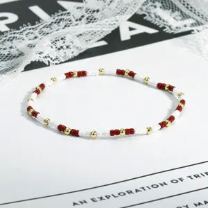 Nahaufnahme des feinen rot-weiß-goldenen Perlenarmbands auf schlichtem weißem Untergrund.