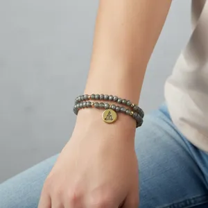 Vista detallada de la pulsera de cuentas grises de doble capa con colgante dorado y motivo.