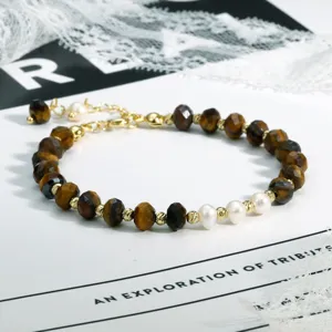 Detailopname van boheemse kralenarmband met tijgeroosten, parels en gouden tussenstukken.