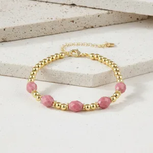 Detailopname van een goudkleurige kettingarmband met glimmende kralen en roze gefacetteerde stenen.
