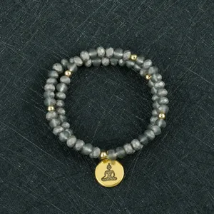 Primer plano detallado del brazalete multicapa de cuentas de vidrio gris con colgante.
