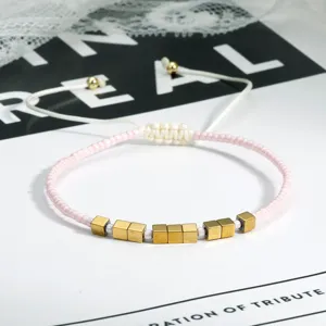 Boho roze kraaltjes armband met gouden kubussen en verstelbaar wit koord detail.