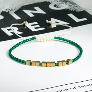 Close-up detail van groene kraal gevlochten armband met goudkleurige kubus kralen en trekkoord.