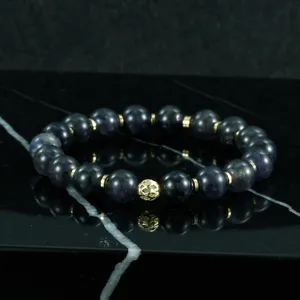 Primer plano detallado de una pulsera de cuentas de piedra oscura con espaciadores dorados.
