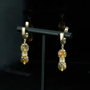 Detalle de cerca de pendientes colgantes dorados de estilo vintage con cuentas ámbar.