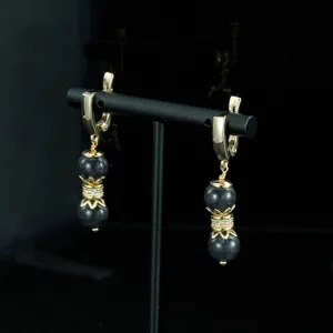 Primer plano de pendientes colgantes dorados vintage con cuentas oscuras y cristales.