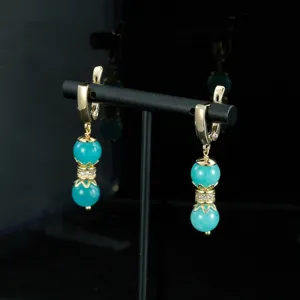 Primer plano de elegantes pendientes dorados con cuentas azules y detalles de cristal.