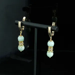 Primer plano de pendientes dorados estilo vintage con perlas verde claro y brillantes estrases.