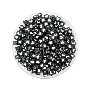 Detailed closeup of black square acrylic beads featuring white heart patterns for jewelry making.