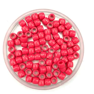 Close-up detail of solid pink plastic barrel beads in a clear container for DIY crafts.
