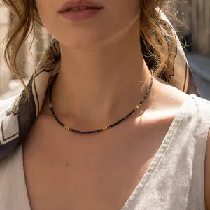Close-up detail shot of a delicate black and gold beaded necklace worn on neck.