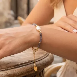 Elegant zoetwaterparel en grijze kralen armband met gouden ketting en hanger detail.