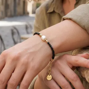 Close-up detail van zwarte kralenarmband met zoetwaterparel en stijlvolle liefdesmunt bedel.